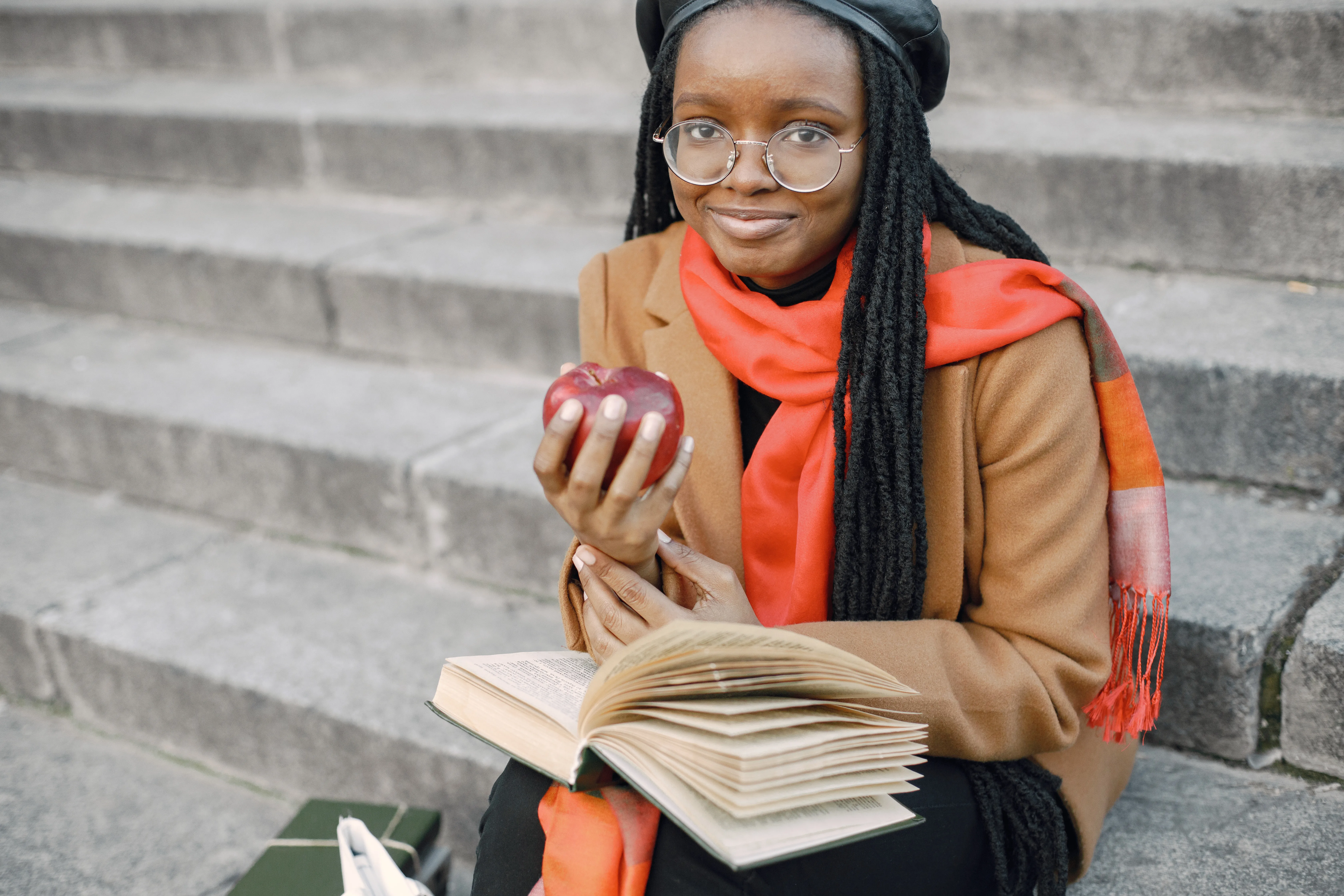 young-black-woman-with-long-locs-hairstyles-sitting-stairs-with-book-woman-wearing-brown-coat-orange-scarf-black-hat